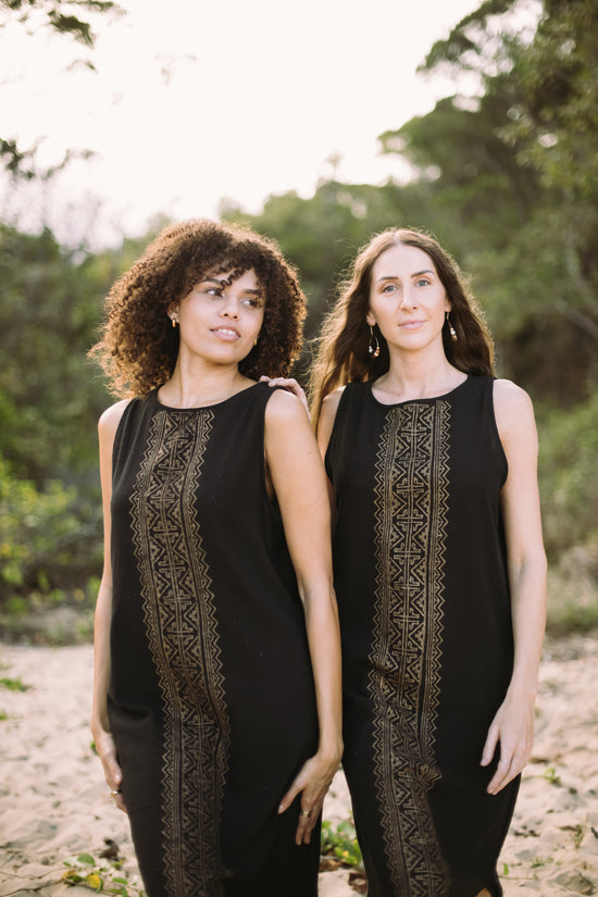 Two women wearing black sleeveless tops with lace details standing outdoors.