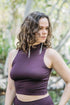 A person wearing a plum purple, high-necked, sleeveless yoga top with a tie-at-the-chest detail.