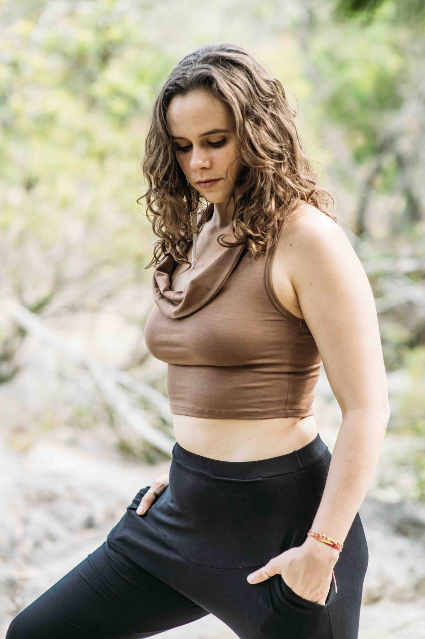 A woman wearing a brown cowl neck tank top and black pants, standing outdoors.