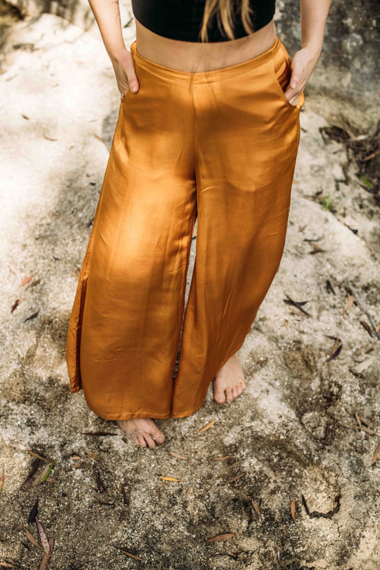 A person standing on a beach wearing high-waisted orange silk pants with pockets.
