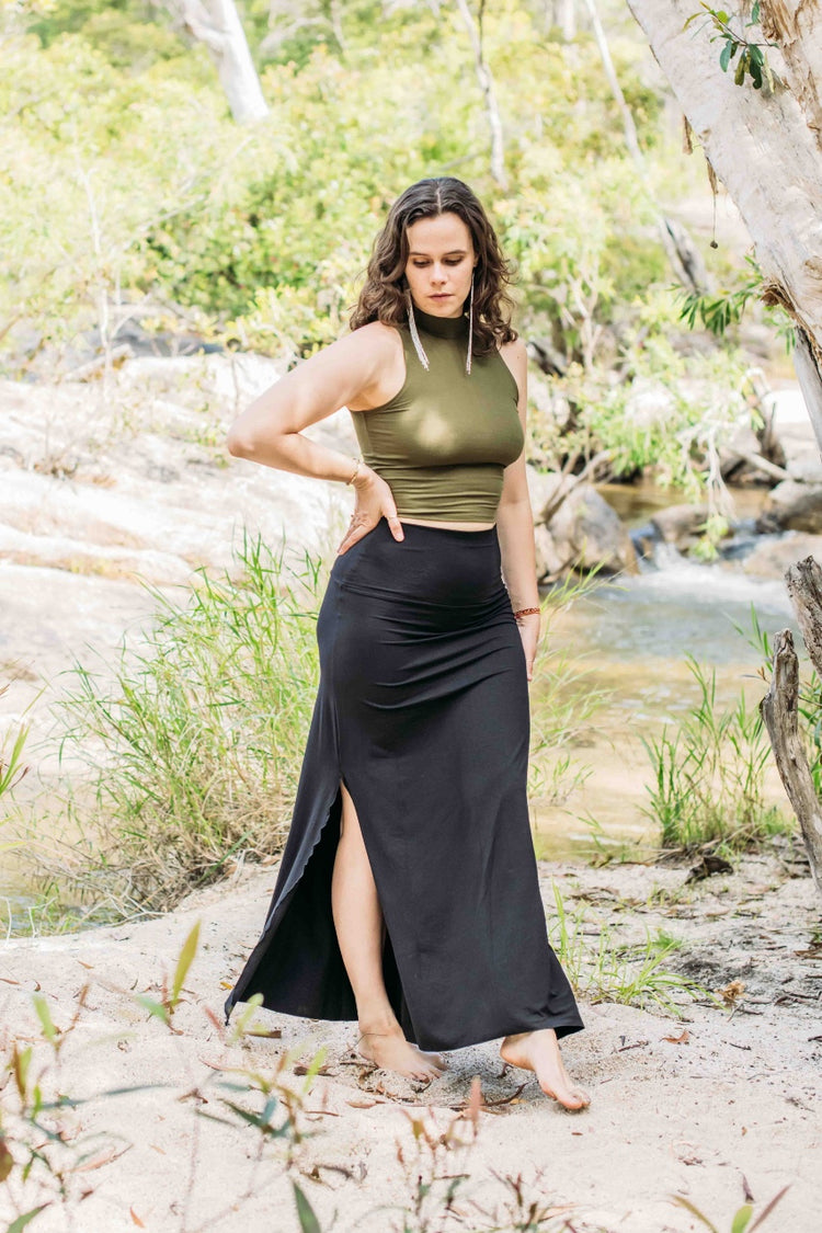 Woman in green top and black skirt standing outdoors near a stream