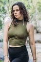 A woman wearing a green, high-necked, sleeveless yoga top and black pants, standing in a natural outdoor setting.