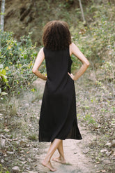 Person wearing a black sleeveless dress walking on a forest path.
