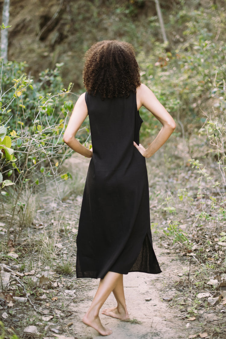 Person wearing a black sleeveless dress walking on a forest path.