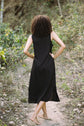 Person wearing a black sleeveless dress walking on a forest path.