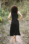 Person wearing a black sleeveless dress walking on a forest path.