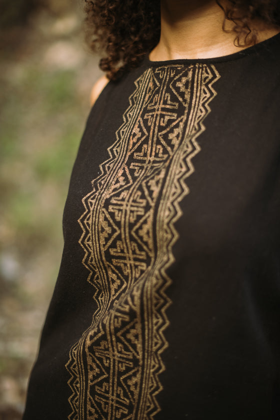 Black garment with gold embroidery on a blurred natural background