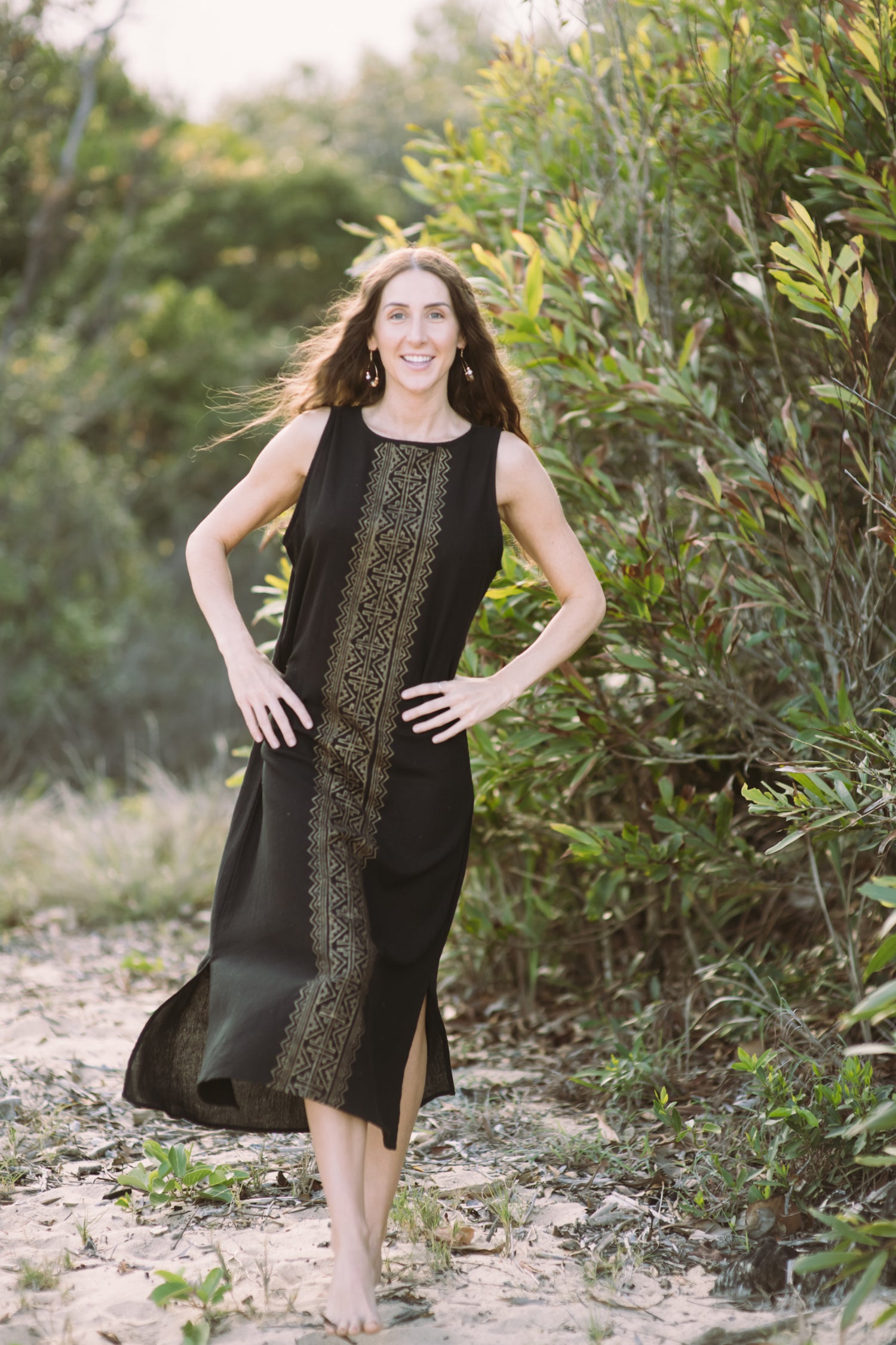 Woman in a black dress with a patterned overlay standing in a natural setting.