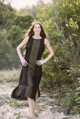 Woman in a black dress with a patterned overlay standing in a natural setting.