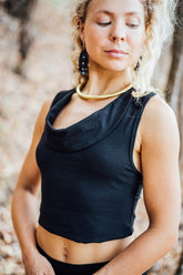 A woman wearing a black cowl neck top with no sleeves, made from stretchy bamboo viscose, in an outdoor setting.