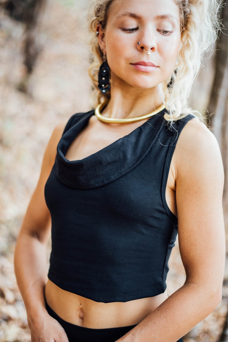 A woman wearing a black cowl neck top with no sleeves, made from stretchy bamboo viscose, in an outdoor setting.